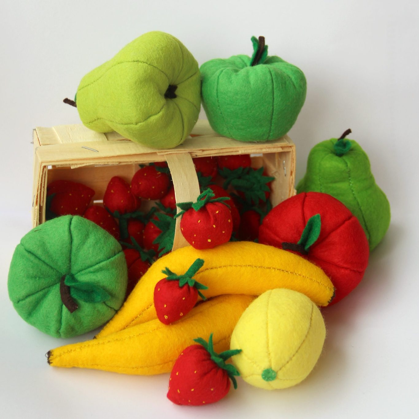 Bunte, weiche Obstspielzeuge in einer Kiste, darunter Äpfel, Bananen und Erdbeeren.