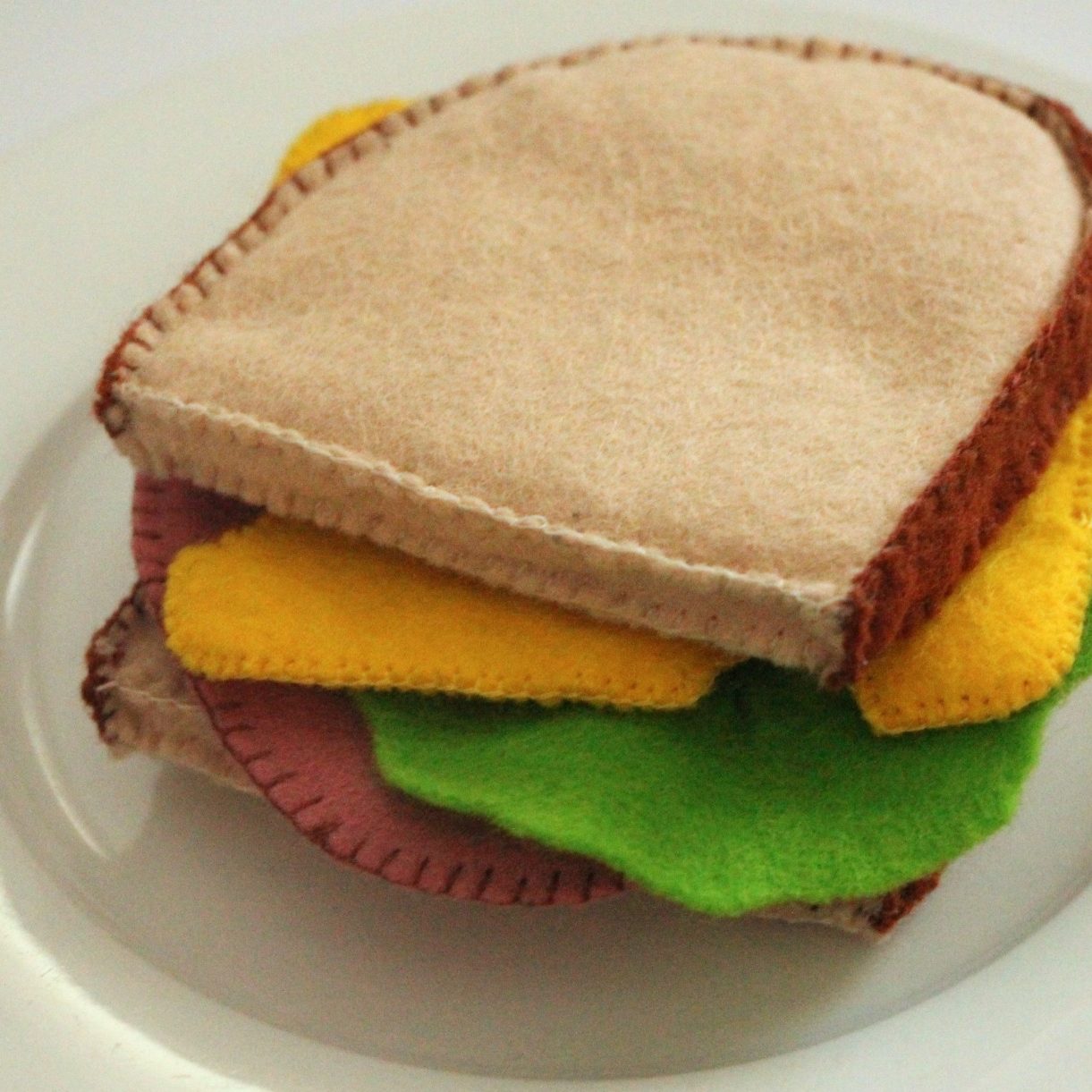 Felt-Sandwich mit Brotscheiben, Käse, Salat und einer Wurstscheibe.